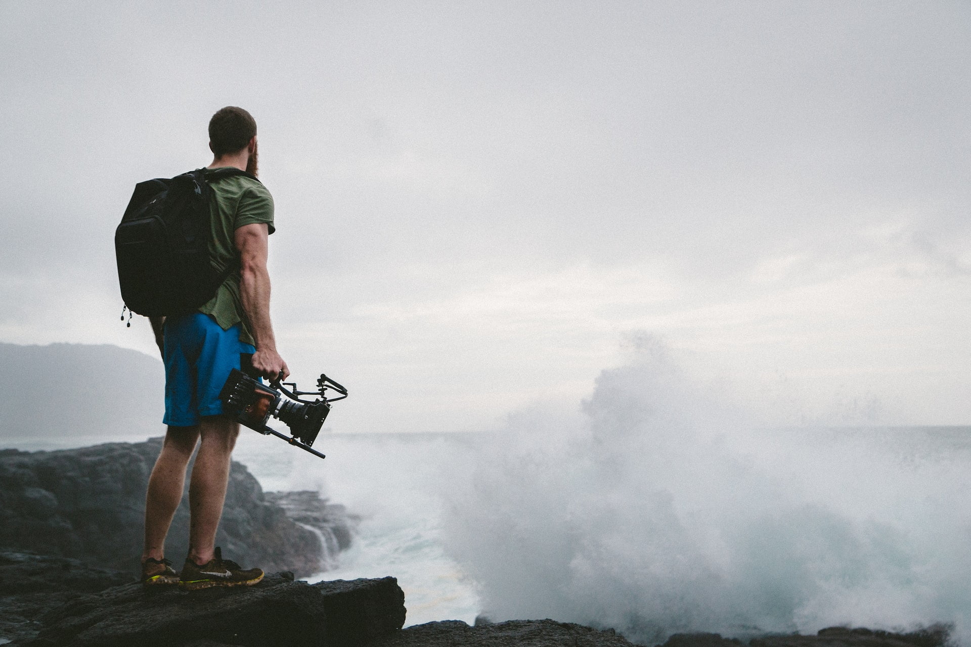 traveler wearing backpack and carrying video camera while looking at the ocean